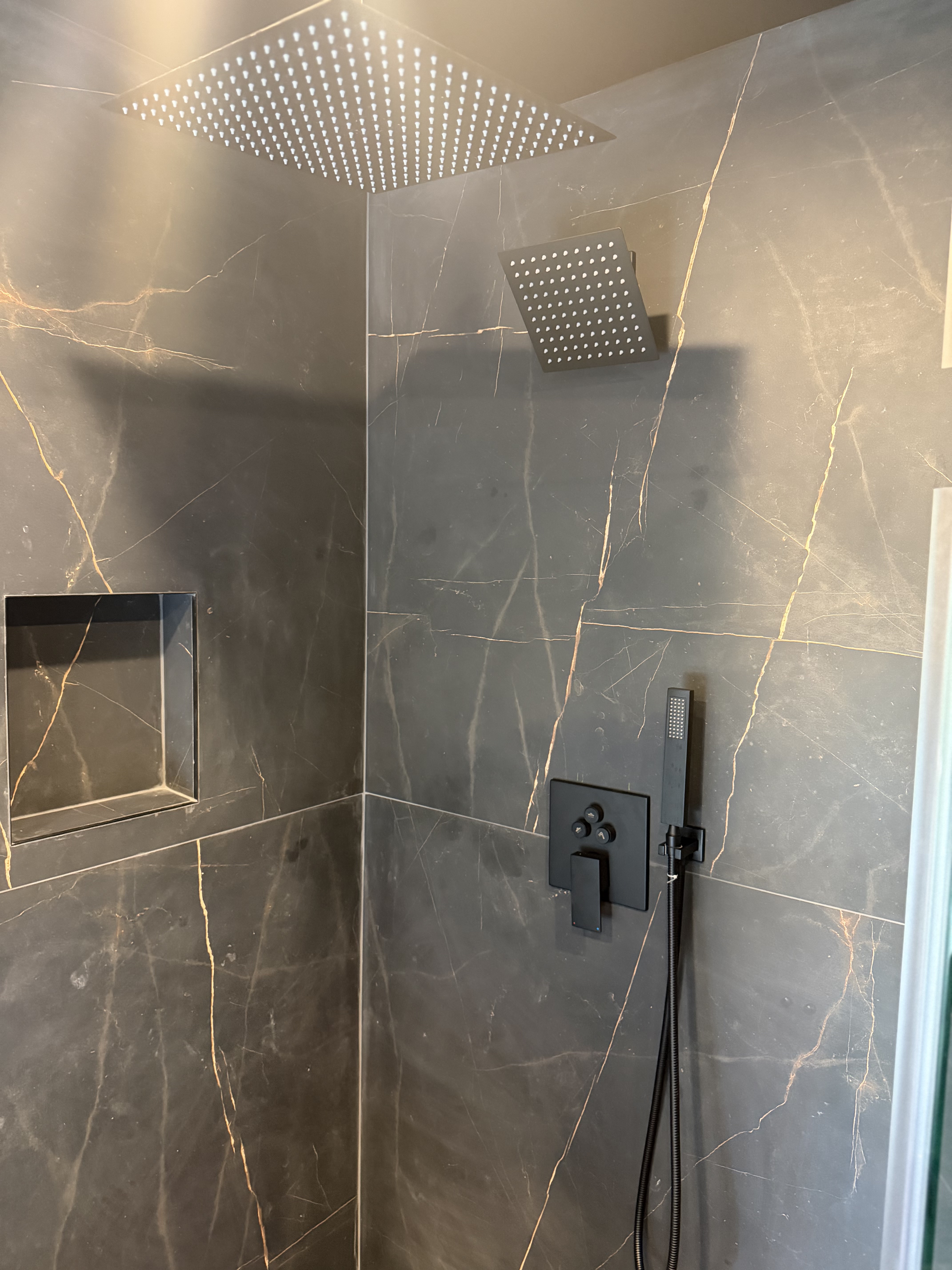 Walk-in shower with rain shower head and black tile in a luxury bathroom remodel